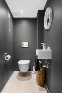 Toilette und Waschbecken in weißer Keramik vor schwarzen Wänden und und einem hellen Boden; sehr kontrastreich