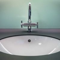 Weißes Keramikwaschbecken eingelassen in einen schwarzen Waschtisch mit einer silbernen Armatur vor blassgrüner Wand